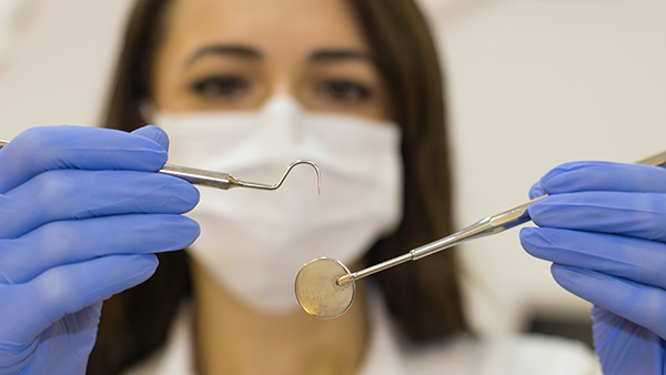 A hygienist holding a dental mirror and pick.