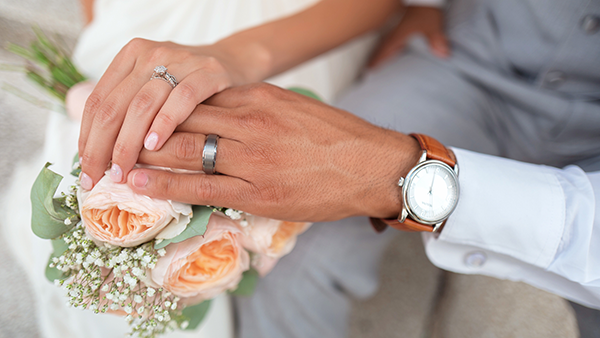 A bride and groom with their hands on a bouquet of flowers.