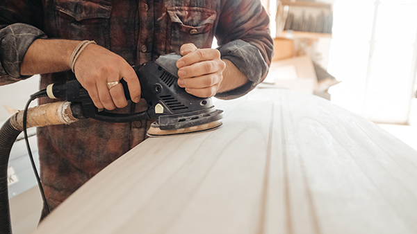 A carpenter with a sander working on a piece of wood.