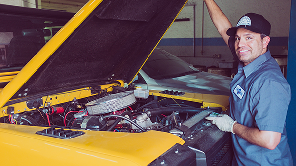 A mechanic in front of a car with the hood up.