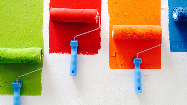 Paint rollers painting multiple colors on a wall.