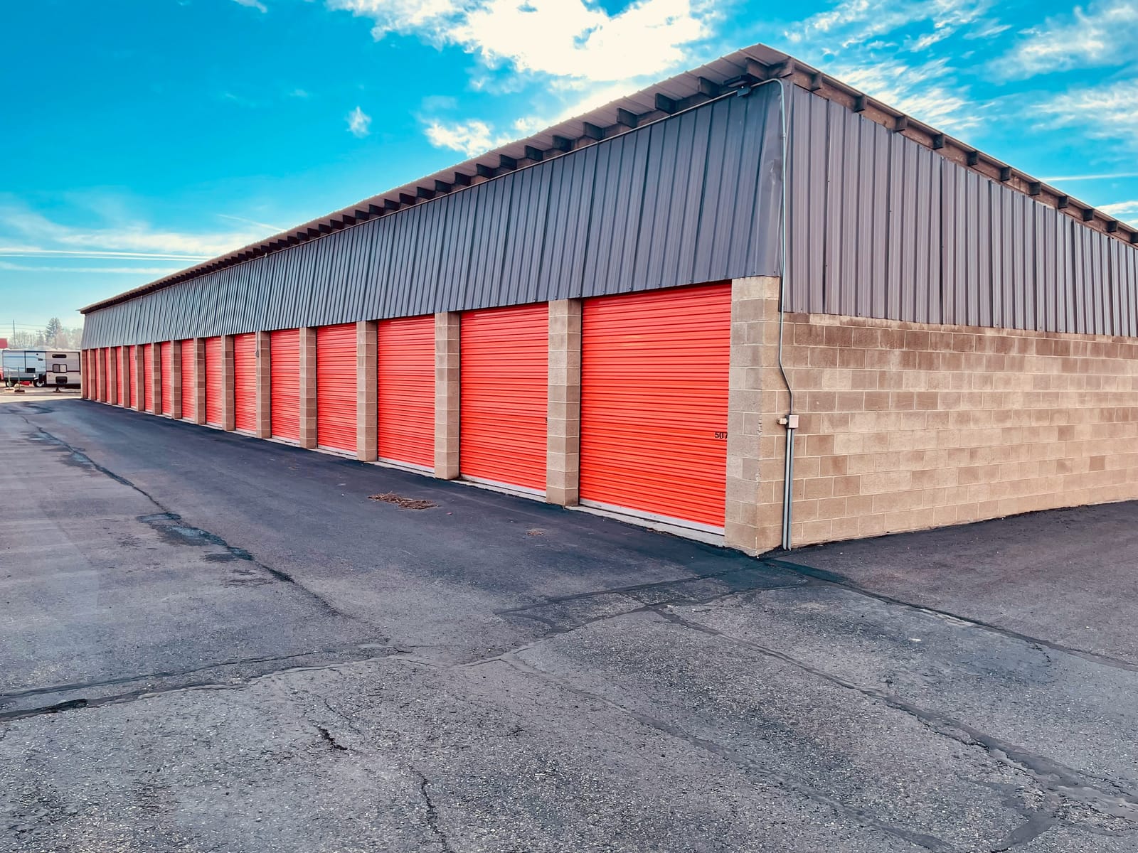 Rows of drive-up self-storage units with orange roll-up doors and RVs parked in the background